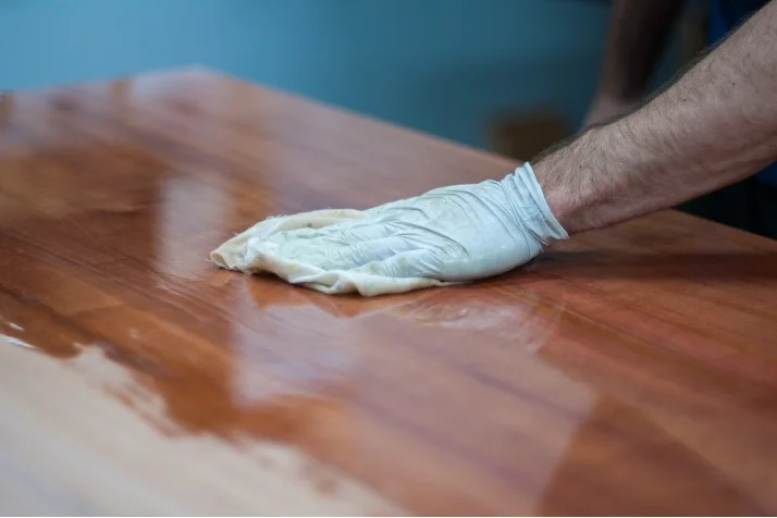 Person trägt Lack auf Holztisch auf